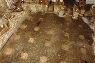 Salle carrée qui montre les vestiges de thermes antiques avec des briques, un sol en terre avec des traces  - Agrandir l'image 1 sur 3, fenêtre modale