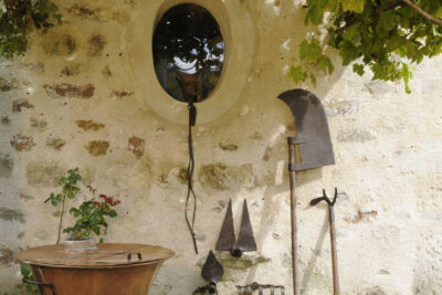 Ensemble d'outils de vigneron représentés les uns à côté des autres dans un décor extérieur, posés sur un mur de pierre et des vignes - Agrandir l'image 4 sur 6, fenêtre modale